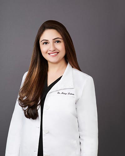 The image shows a woman wearing a white coat with black text on it, standing against a light background.
