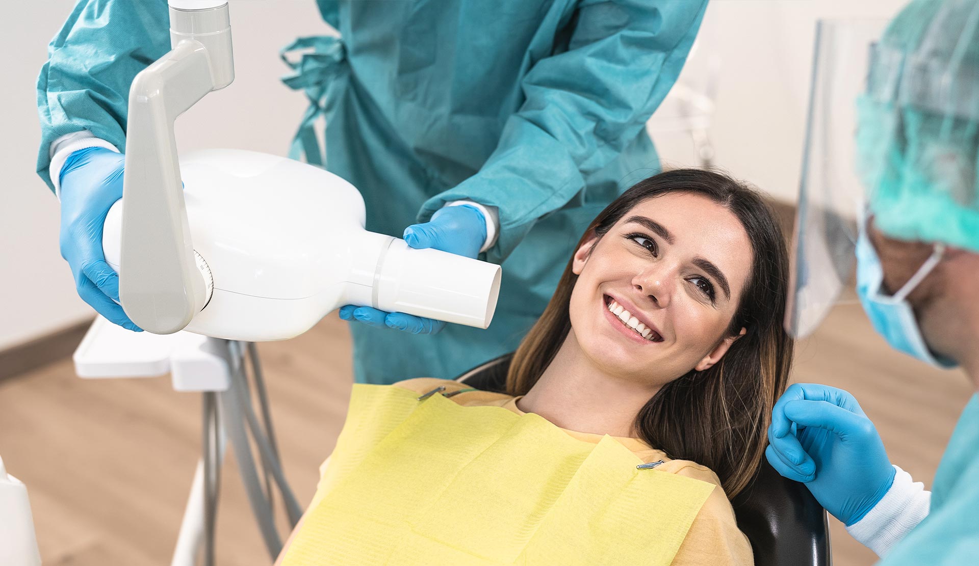 Woman seated in dental chair with hygienist performing cleaning procedure.