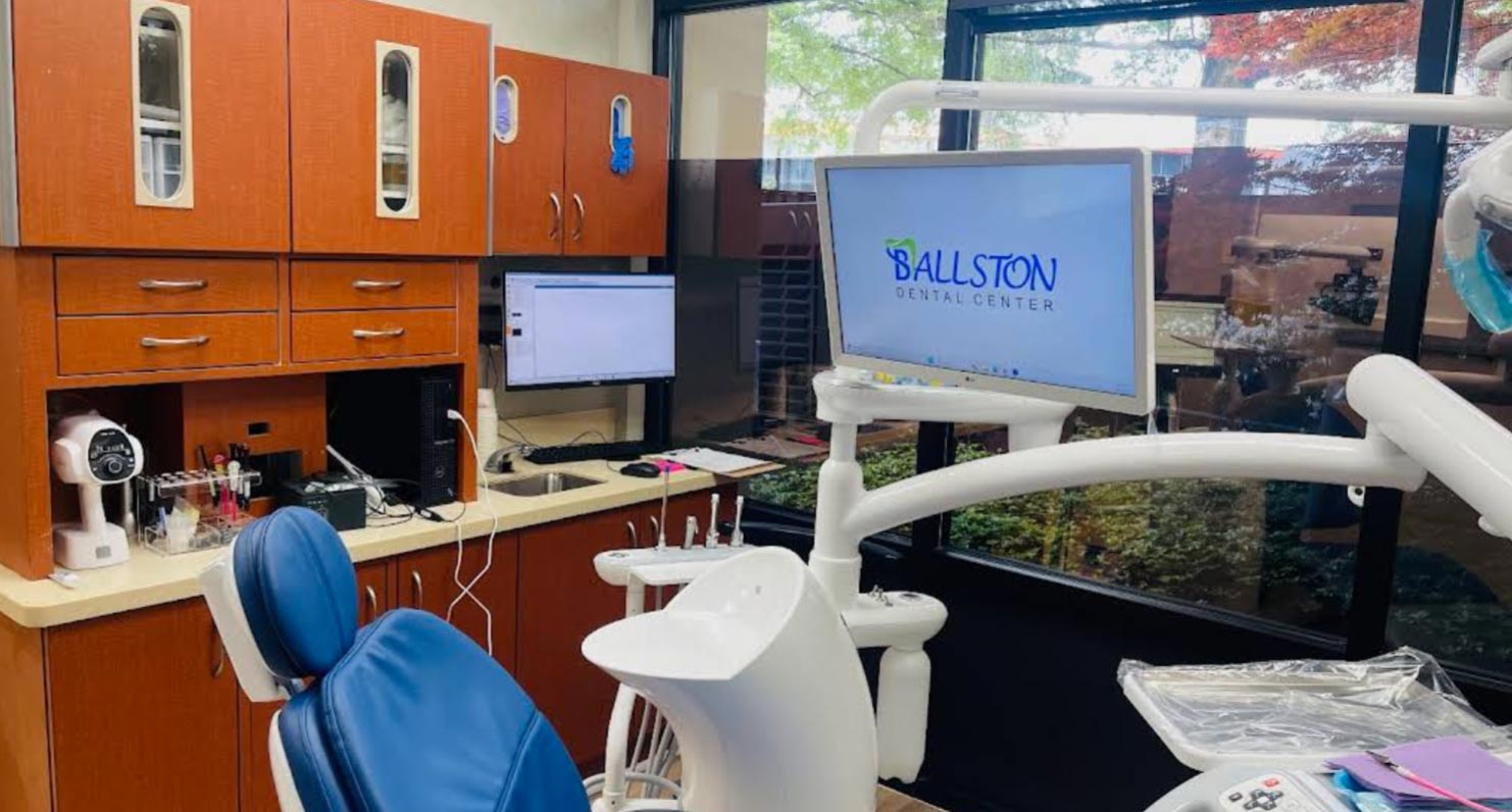 The image shows a dental office interior with a modern dental chair, a computer monitor displaying  Ballston Dental,  and various dental equipment in the background.