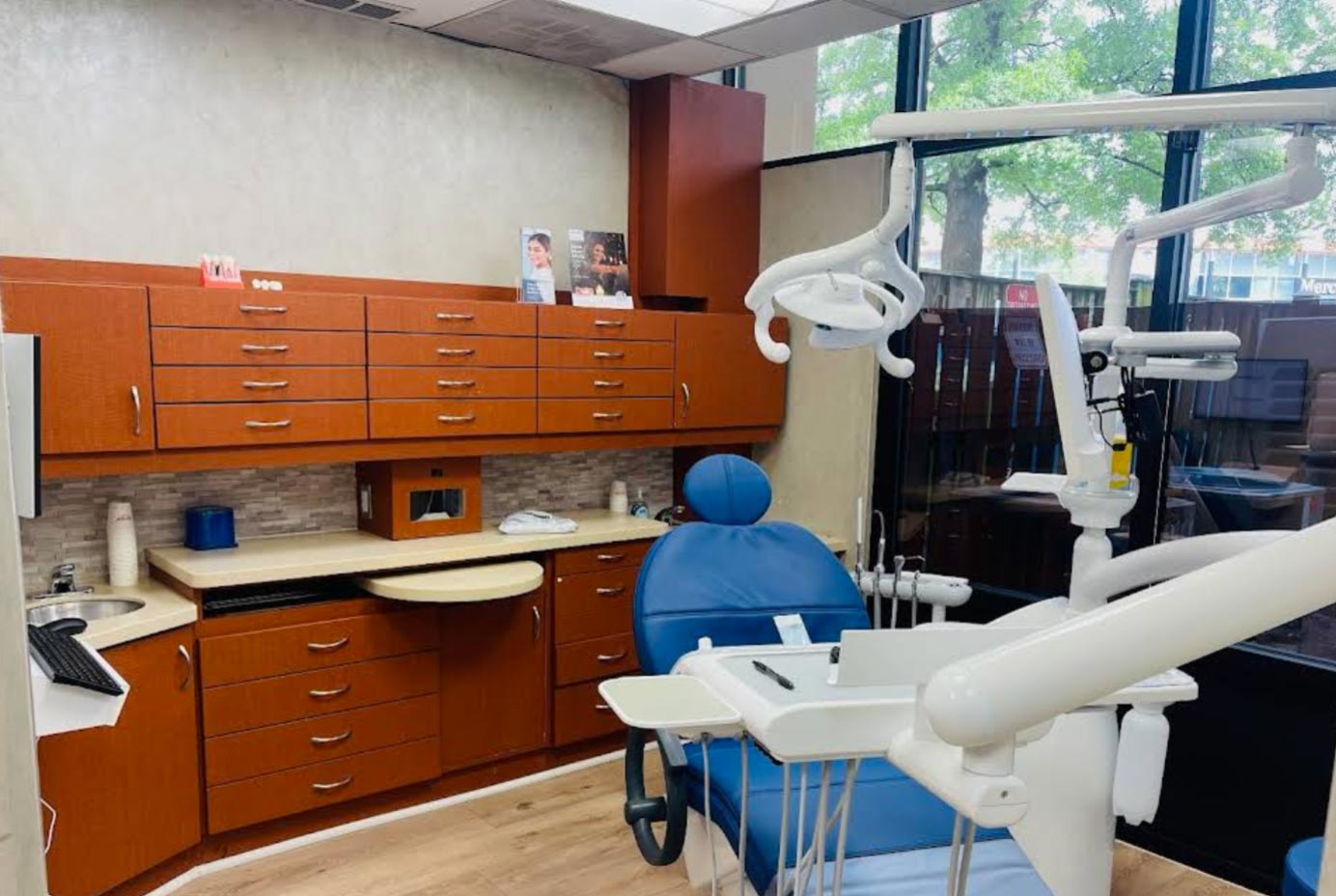 The image shows an interior view of a dental office with modern furnishings including chairs, cabinets, and equipment such as a dental chair, sink, and various dental tools.