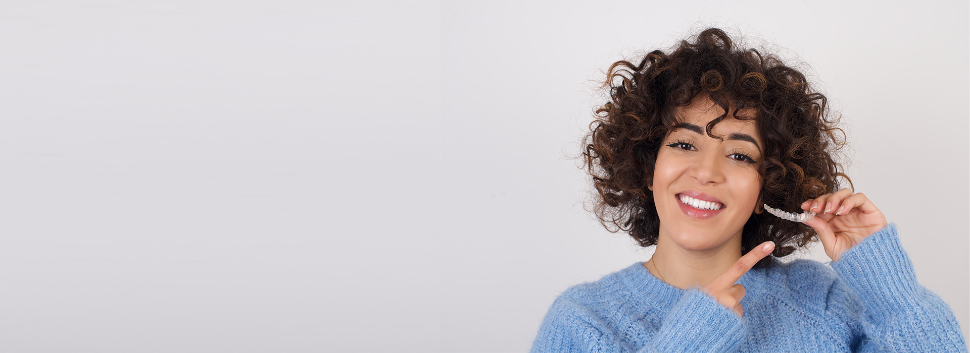 A woman with curly hair smiling at the camera while holding a toothbrush.