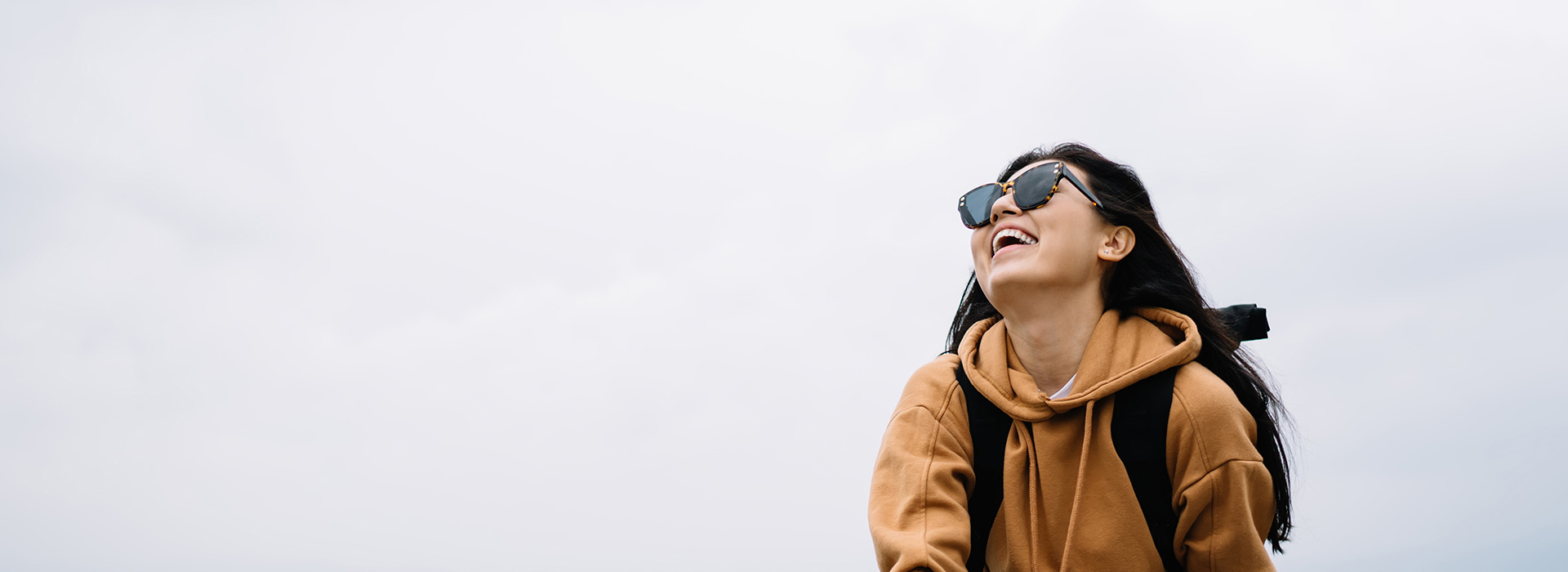 A person wearing sunglasses and a backpack is standing against a gray sky background.