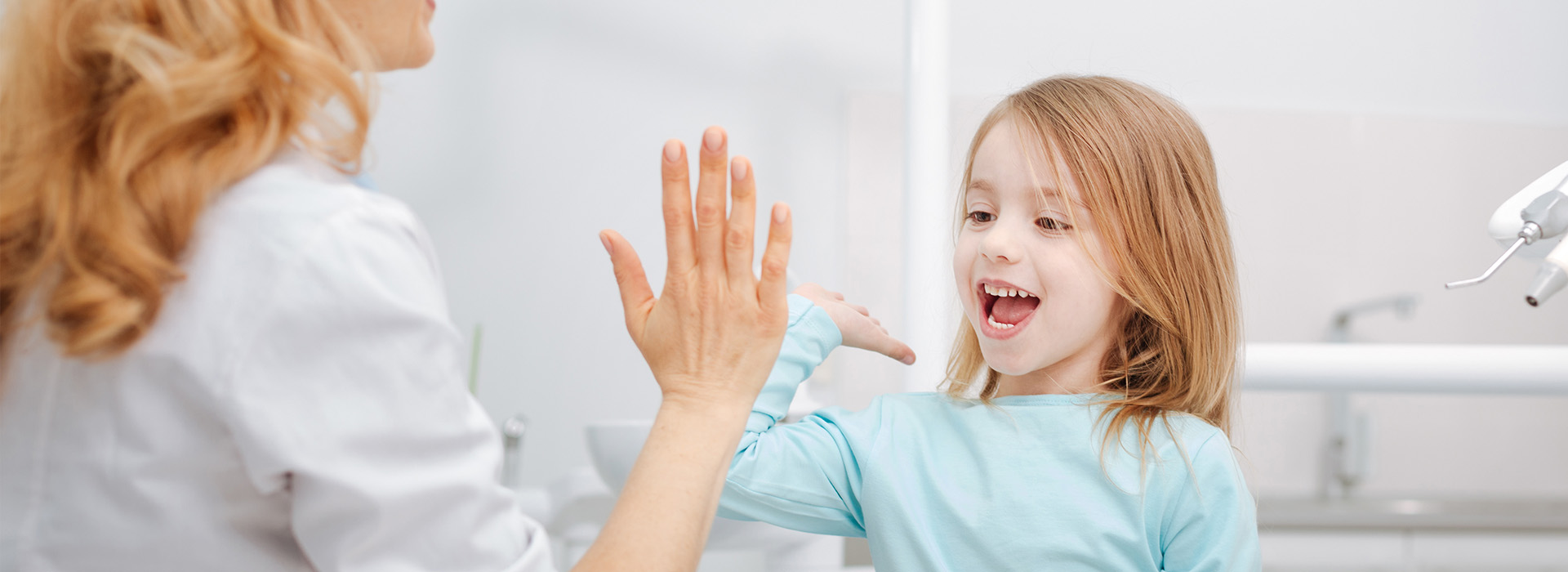 The image shows a young girl reaching up with her hands towards an adult s face, possibly interacting playfully, against a backdrop of a bathroom setting.