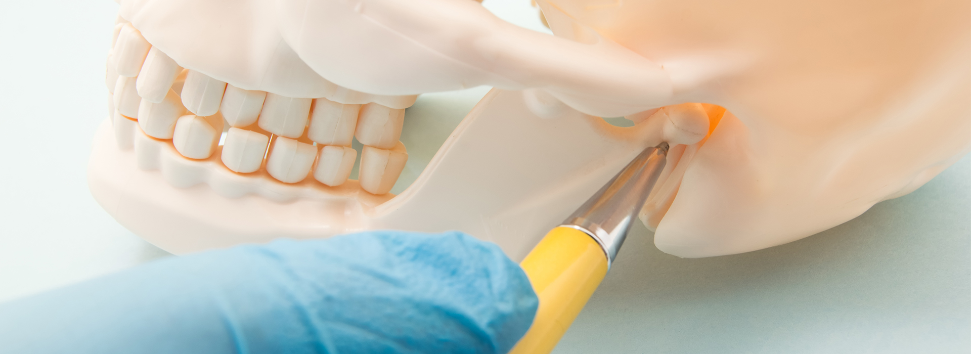 The image shows a close-up view of a human tooth being held by a pair of tweezers while lying on a dental work surface, with a focus on the tooth and tweezers, and a blurred background that suggests a dental office setting.