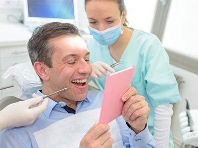 A dentist showing a patient a pink cardboard model of their teeth during a dental appointment.