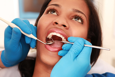 A woman receiving dental treatment, with a dentist performing oral surgery on her, surrounded by dental instruments and tools.