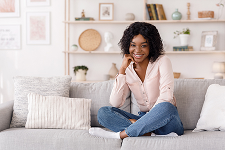 A woman sitting on a couch with her legs crossed, smiling at the camera.