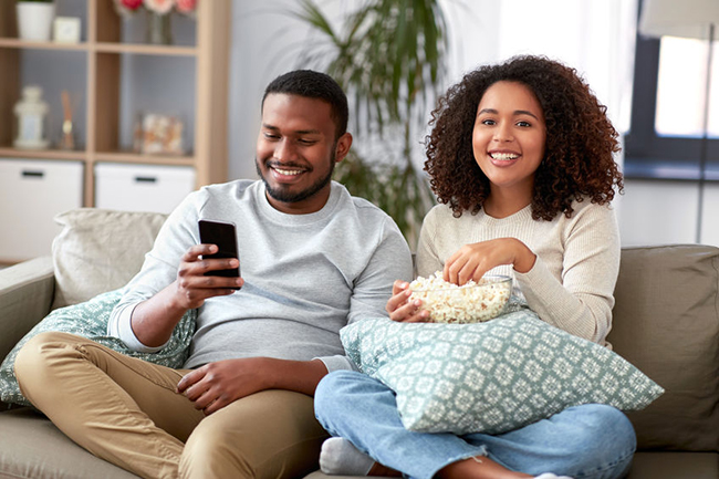 A man and woman sitting on a couch, sharing a moment while enjoying some popcorn, with a warm and relaxed atmosphere.
