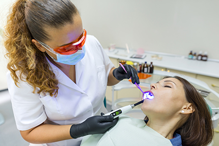 A dental hygienist performing teeth whitening on a patient in an office setting.