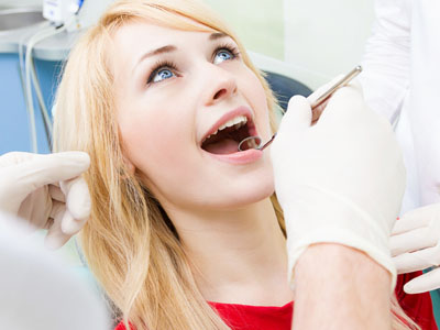 Woman receiving dental treatment with dentist's hands visible, wearing red shirt and blue gloves.