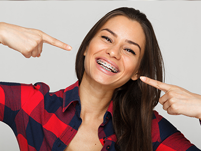 The image features a woman with a playful expression pointing at her teeth, set against a white background.