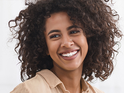 The image shows a smiling woman with curly hair, wearing a light-colored top, set against a neutral background.